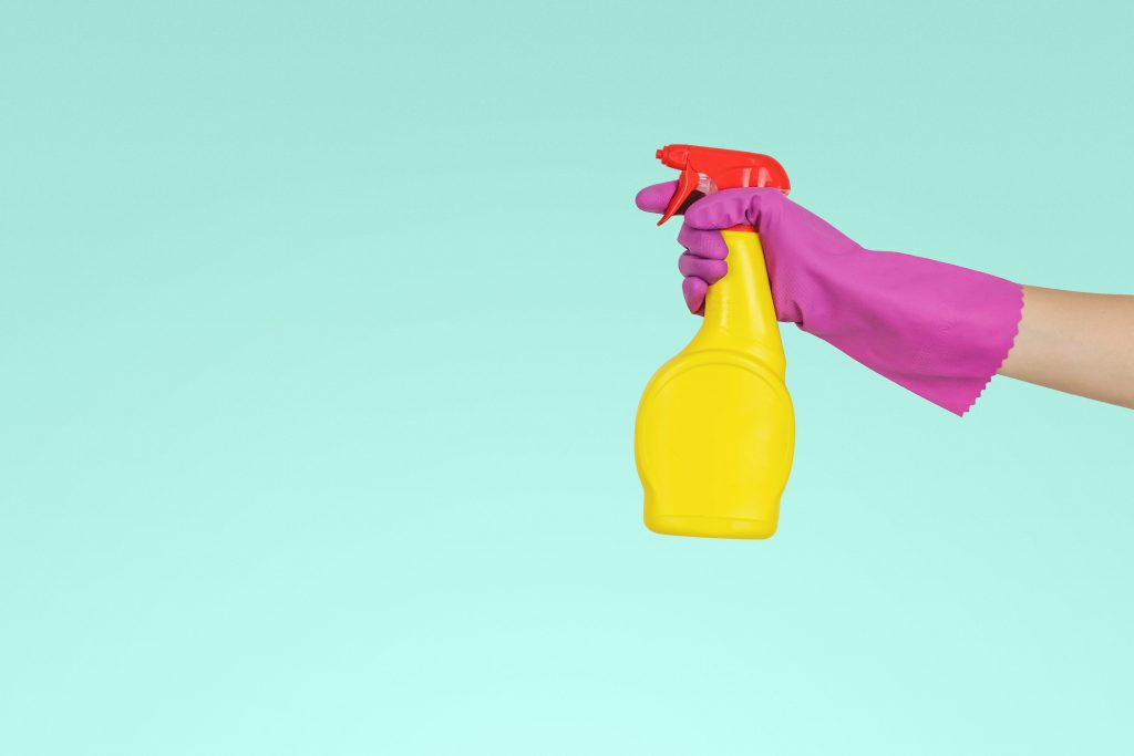 A woman's gloved hand holding a spray bottle in order to clean the house