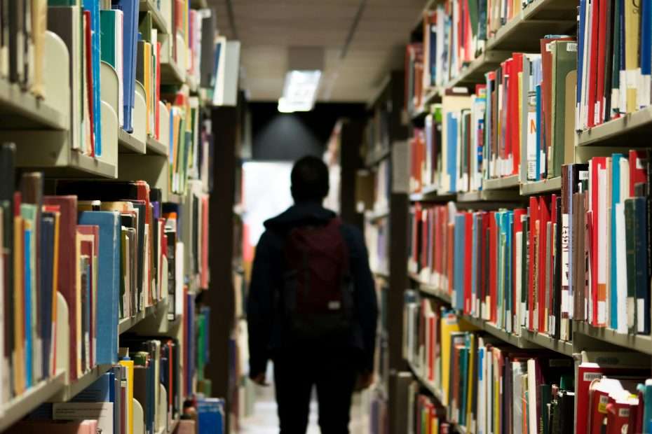 silhouette of a person with a backpack in a library aisle