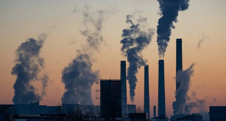 Factory chimneys releasing dense smoke into the sky at sunset, symbolizing ongoing emissions despite net-zero claims.