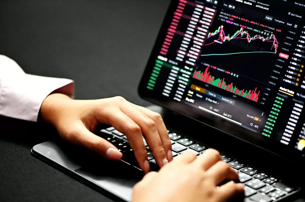 Hands typing on a laptop displaying cryptocurrency and stock trading graphs, symbolising the dominance of money metrics in decision-making without multicapital consideration.
