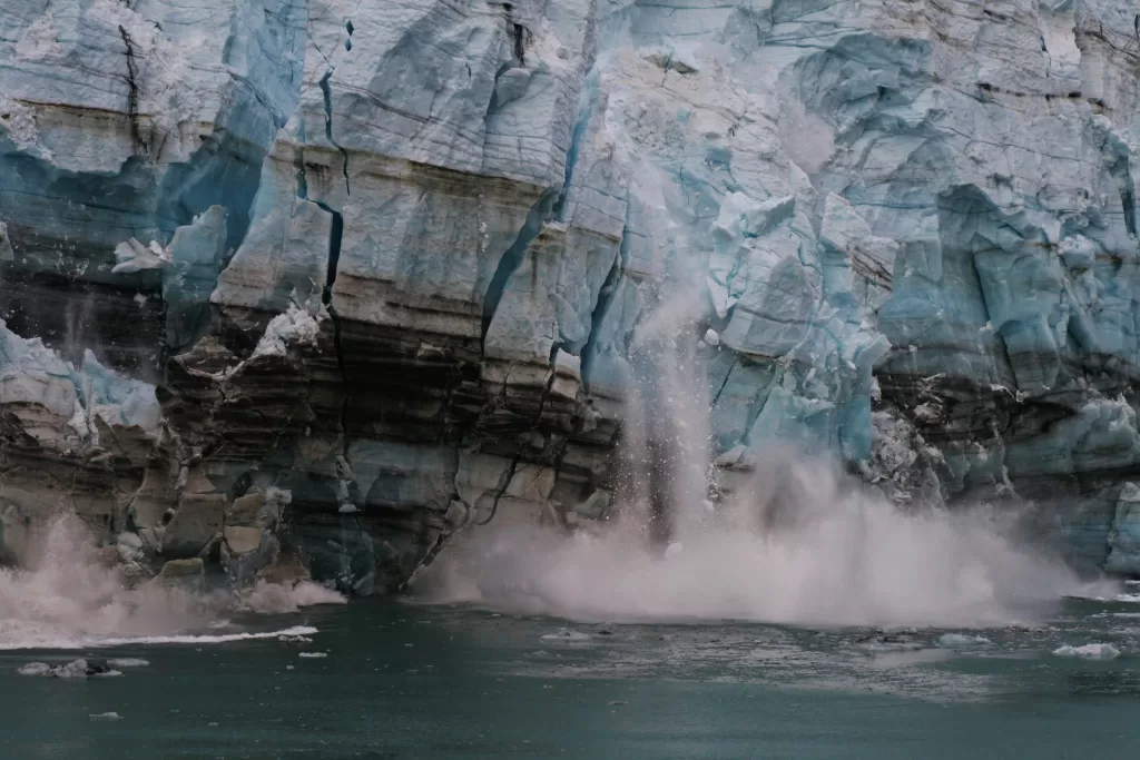 Close-up of a glacier calving into the ocean, with ice breaking and crashing into water, symbolizing climate change and the need for regenerative behavioral shifts.