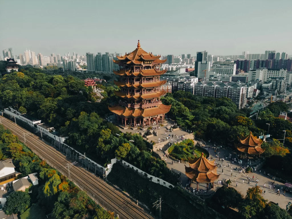 Aerial view of Wuhan’s Yellow Crane Tower surrounded by trees and urban development, illustrating the intersection of cultural heritage and modern urbanization.