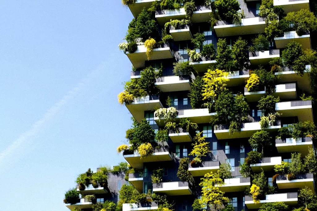 Tall building covered with trees and plants growing on balconies, demonstrating vertical gardens integrated into urban architecture.