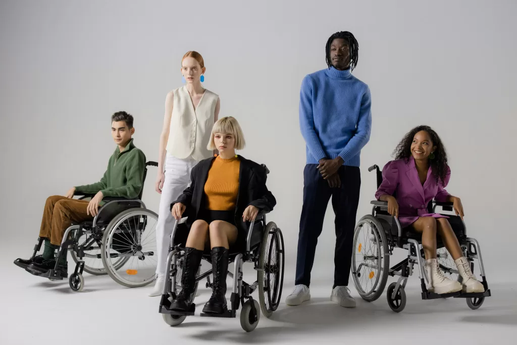 5 people in colourful outfits, 2 stand and 3 use wheelchairs